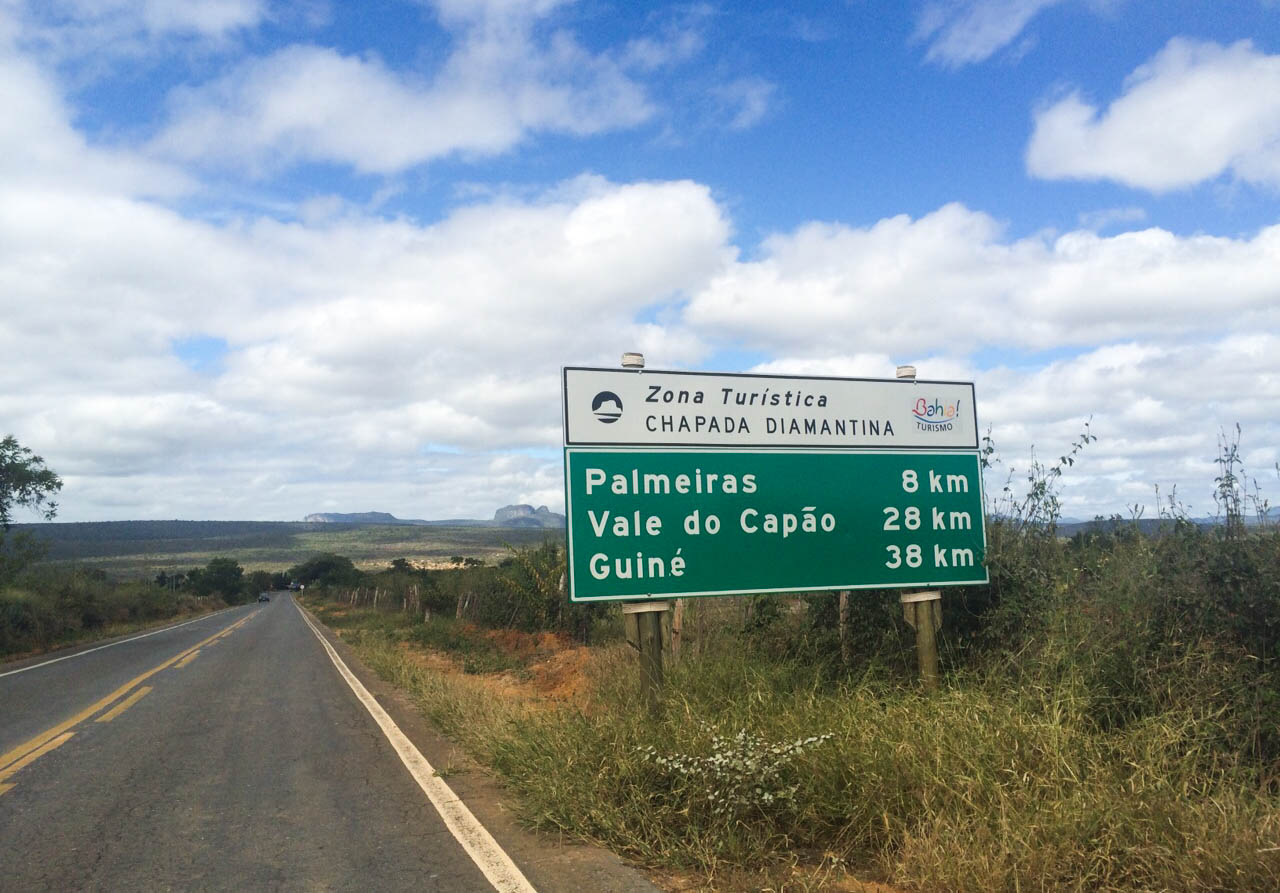  A green highway sign for the Chapada Diamantina Tourist Zone indicating distances to Palmeiras, Vale do Capão, and Guiné. 
