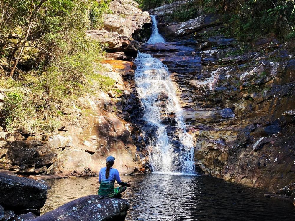 A woman sitting peacefully on a rock by the natural pool at the base of the 30-meter-high Funis Waterfall. 