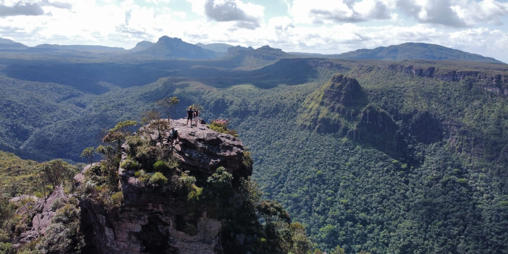 Hikers standing on a rocky peak at Morro do Castelo, overlooking a vast, forested canyon in Chapada Diamantina.