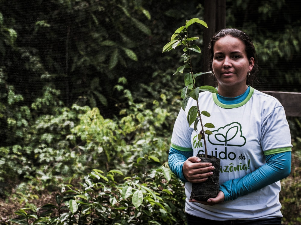 A woman holding a native tree sapling for a sustainability and reforestation project in the Amazon.