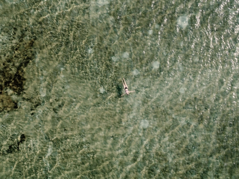 Top-down view of a person swimming in a crystal-clear rainwater lagoon in Lençóis Maranhenses, revealing the sandy bottom. Top-down view of a person swimming in a crystal-clear rainwater lagoon in Lençóis Maranhenses, revealing the sandy bottom.