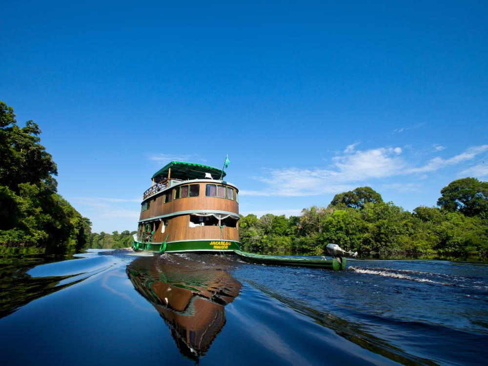  A multi-level traditional wooden river cruise boat navigates the reflective dark waters of the Amazon.