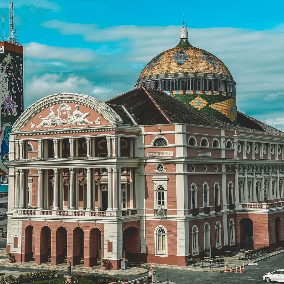 The pink neoclassical facade and colorful tiled dome of the Amazon Theatre in Manaus under a blue sky. The pink neoclassical facade and colorful tiled dome of the Amazon Theatre in Manaus under a blue sky.