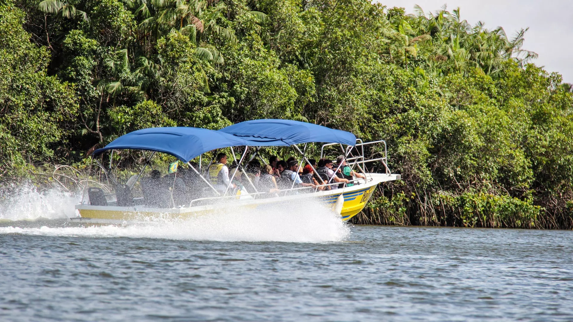  Passengers ride a yellow motorboat with blue canopies along the Preguiças River on their way to Atins.