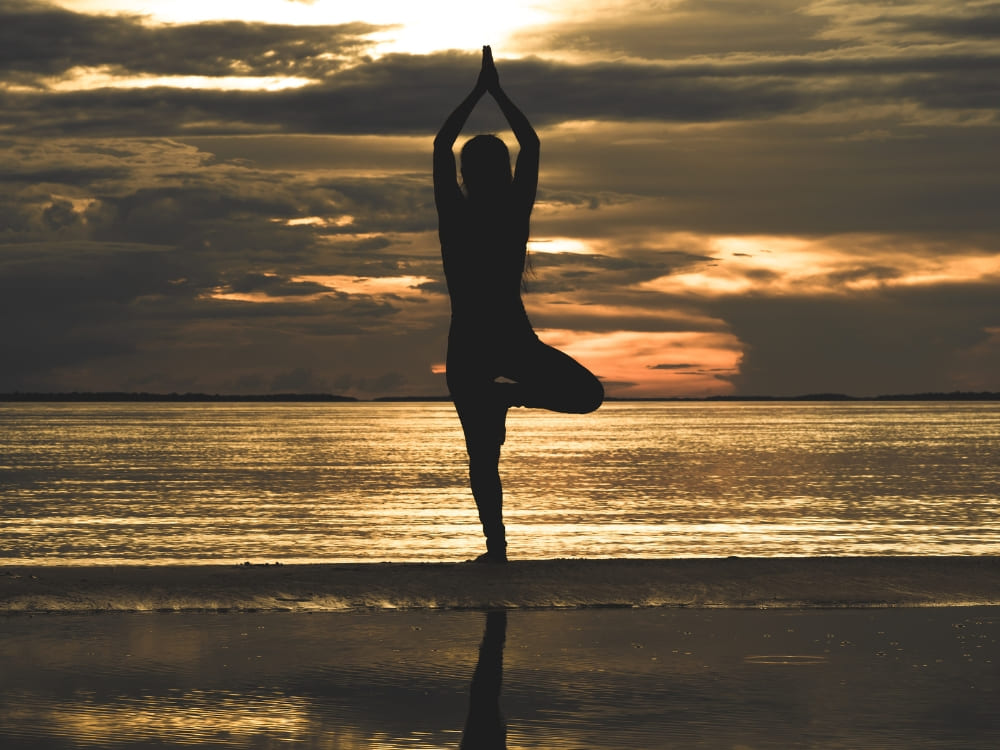 Silhouette of a person doing a yoga tree pose on an Amazon river beach at sunset.