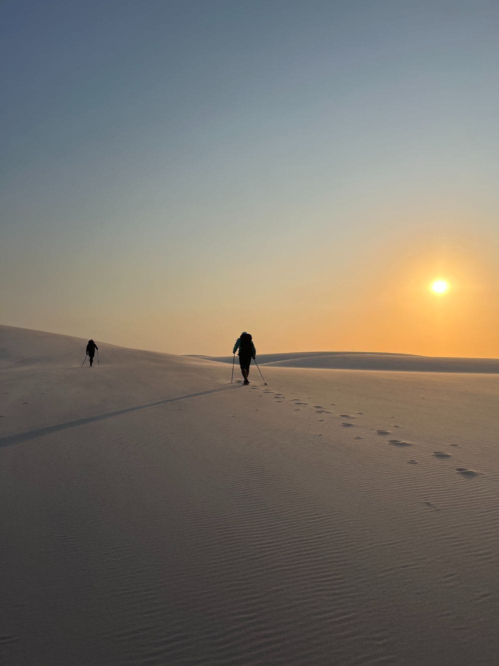 Silhouetted people walk across the sand dunes of Lençóis Maranhenses at sunset.
