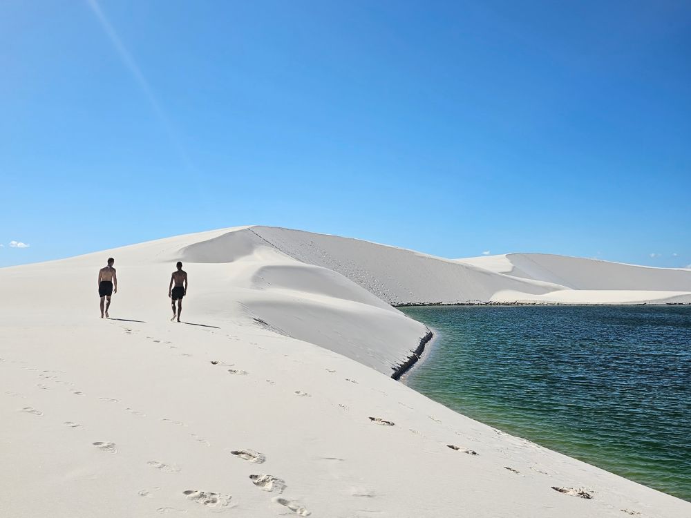 A backpacker walks across the vast white sand dunes of Lençóis Maranhenses National Park under a cloudy sky.