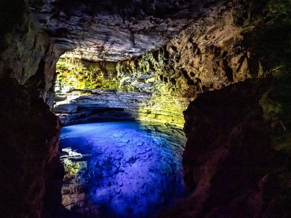 A bright ray of sunlight illuminates the crystal-clear blue water inside the underground limestone cave of Poço Encantado.