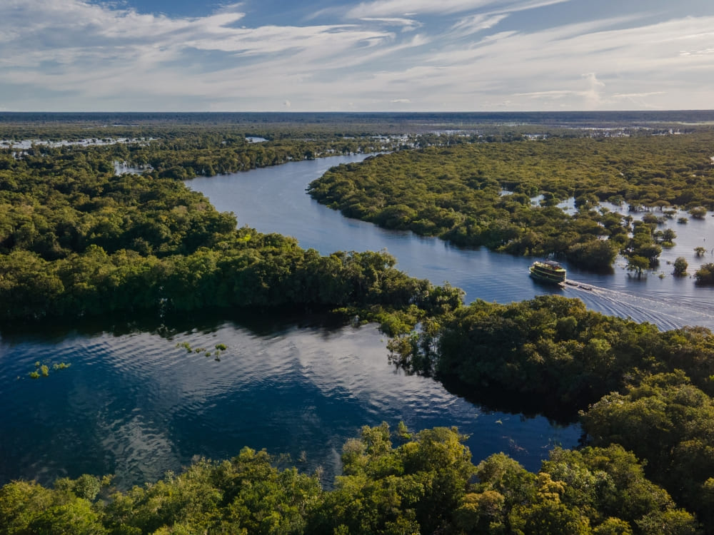 Aerial view of a tour boat navigating a winding river through the lush green landscape of the Amazon.