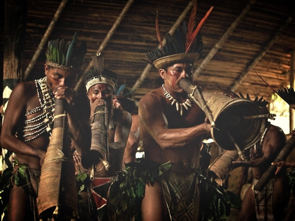 Indigenous men playing traditional wind instruments during a cultural ceremony in the Amazon.
