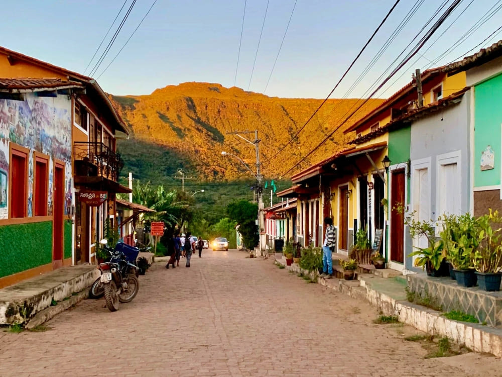Colorful houses lining the peaceful main street of Vale do Capão with a massive mountain glowing at sunset. 