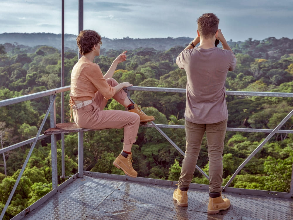 Travelers using binoculars on an observation tower high above the canopy to safely spot birds and wildlife in the Amazon Rainforest.