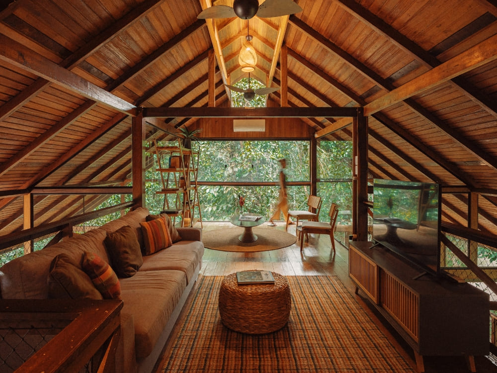 A cozy, rustic interior of a wooden bungalow at an Amazon ecolodge featuring a comfortable living area and a view of the forest. 