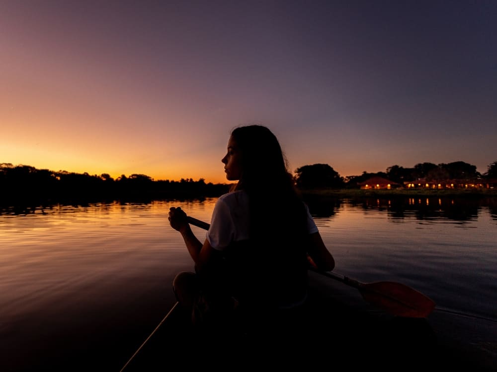 Silhouette of a person paddling a canoe on the calm waters of a river during a peaceful sunset. Silhouette of a person paddling a canoe on the calm waters of a river during a peaceful sunset.