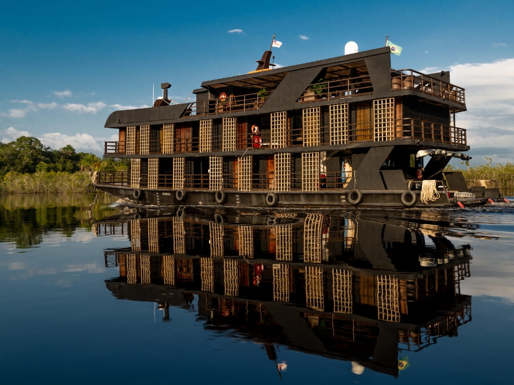 A sophisticated multi-story vessel reflects on the dark water, offering one of the best Amazon river cruises in Brazil. 