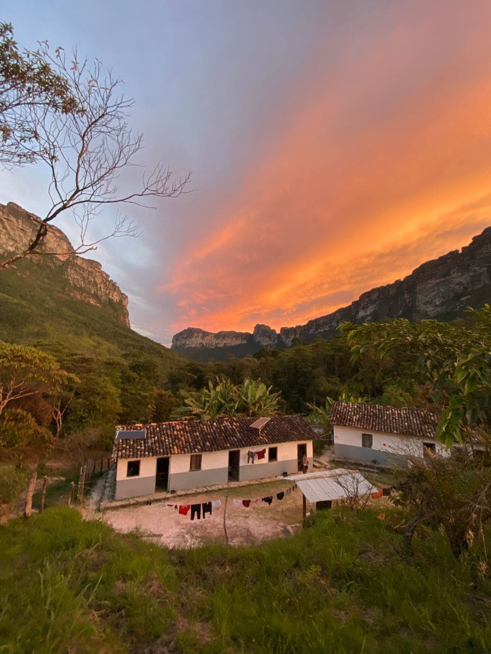 Simple white homestay houses nestled in a valley under a colorful sunset sky during the Vale do Pati trek. 
