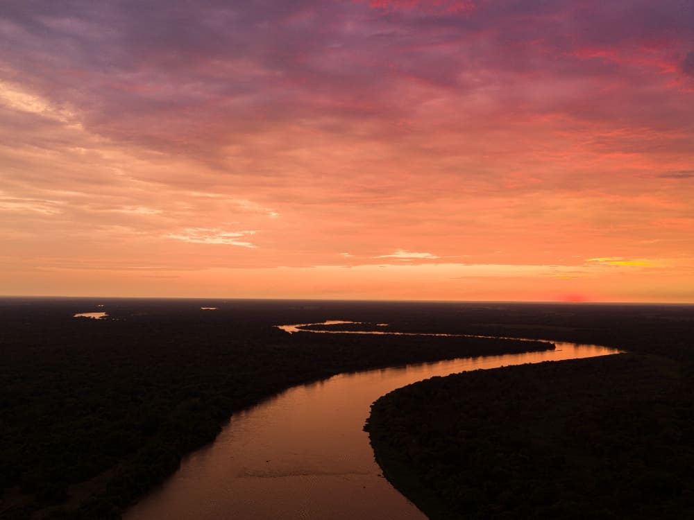 Aerial view of a winding river flowing through the vast wetlands, reflecting the pink and orange evening sky. Aerial view of a winding river flowing through the vast wetlands, reflecting the pink and orange evening sky.