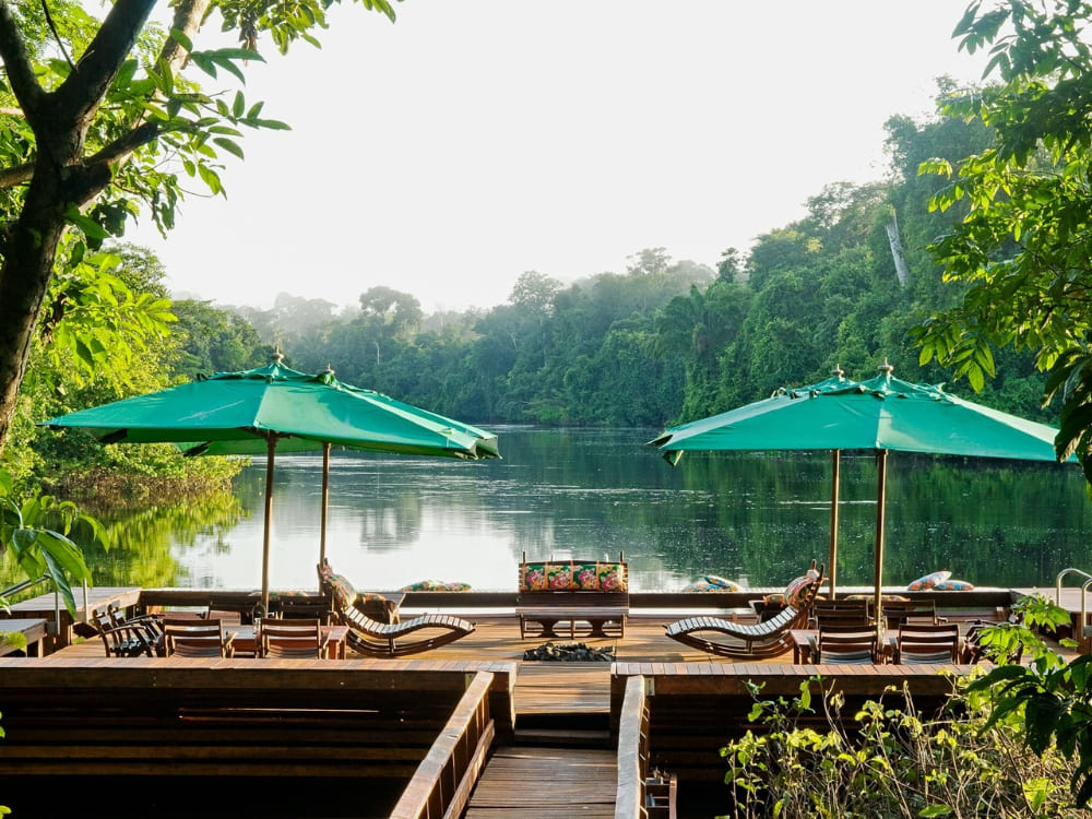 Wooden deck over the water with lounge chairs and large green umbrellas surrounded by trees. Wooden deck over the water with lounge chairs and large green umbrellas surrounded by trees.