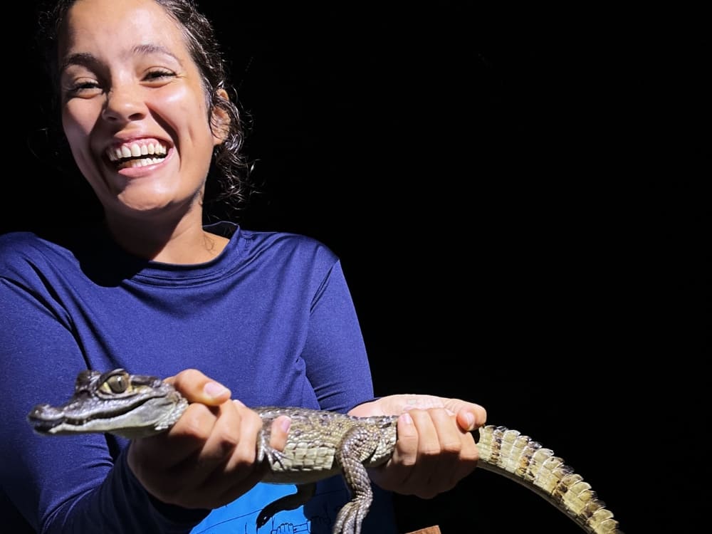 Mariana smiles enthusiastically while safely holding a small alligator during a night excursion in the Amazon. 