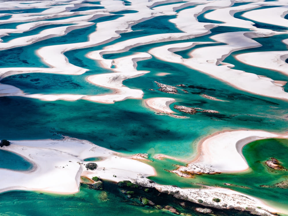 Aerial view of the white sand dunes and green rainwater lagoons in Lençóis Maranhenses National Park. 