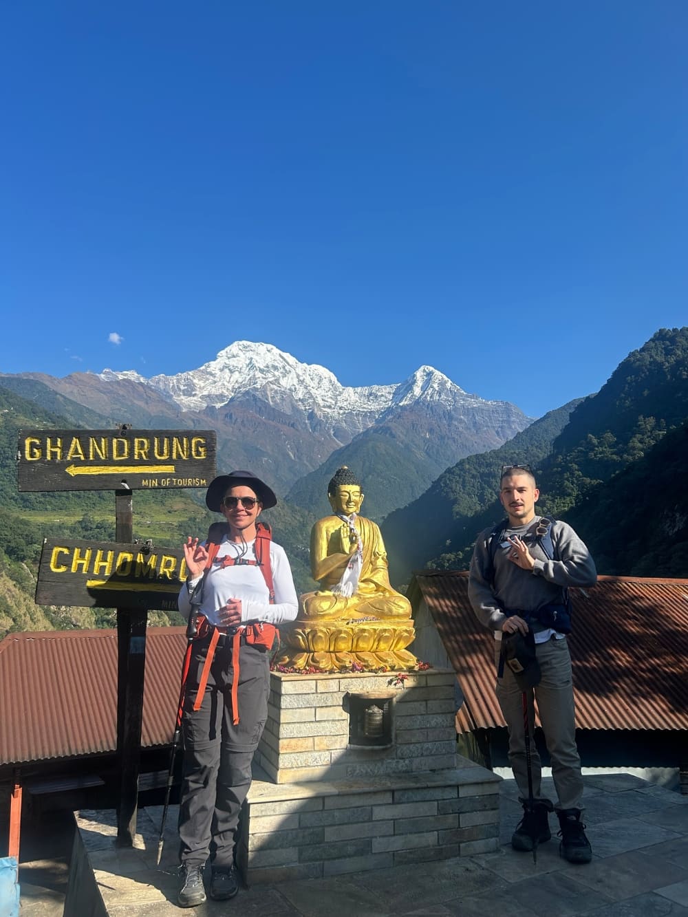 Mila and Lorenzo beside a Buddha statue and trail signs during their sustainable trek in Nepal. Mila and Lorenzo beside a Buddha statue and trail signs during their sustainable trek in Nepal.