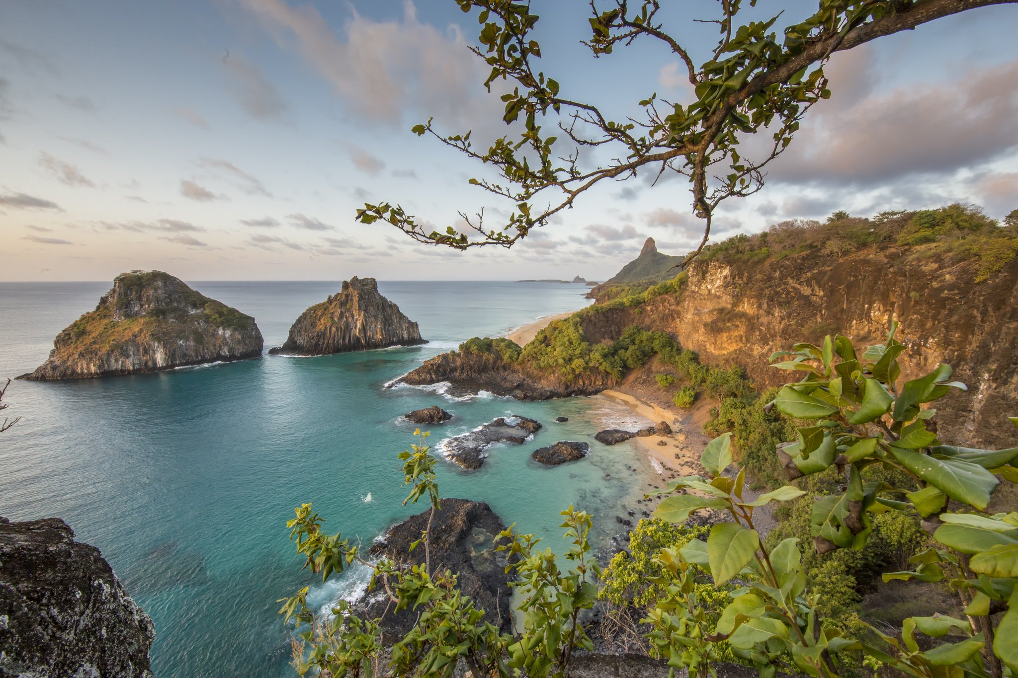 Rocky islets, turquoise bays, and cliffs draped in green — the surface is only the beginning. Aerial view of turquoise coves, golden cliffs and twin rock islets framing the coastline of Fernando de Noronha, the setting for a 2-Day Diving Package in Fernando de Noronha
