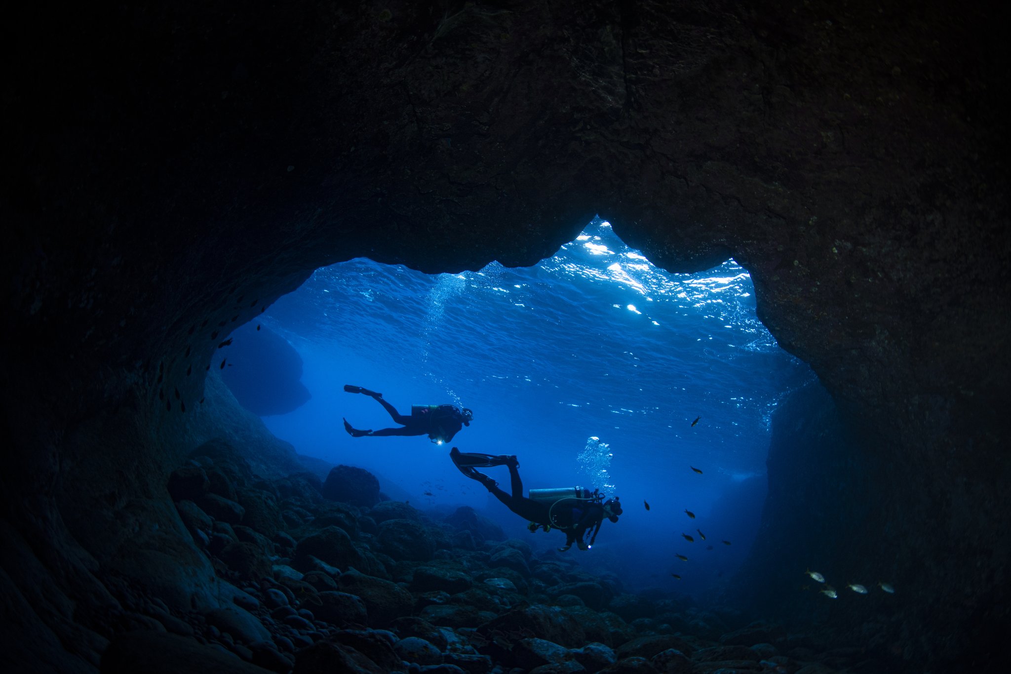 Two divers, one cave, a world of electric blue beyond. Photo: Global_Pics Two scuba divers silhouetted against brilliant blue water inside a rocky underwater cave entrance, part of the 2-Day Diving Package in Fernando de Noronha