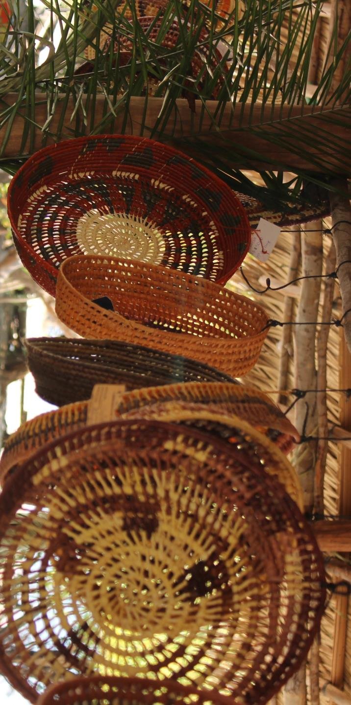Spiral patterns, warm ochres — artisan basketry straight from riverside hands. Handwoven palm-fibre baskets in earth tones hanging from a bamboo structure at a community craft stall visited on an Amazon cruise from Alter do Chão