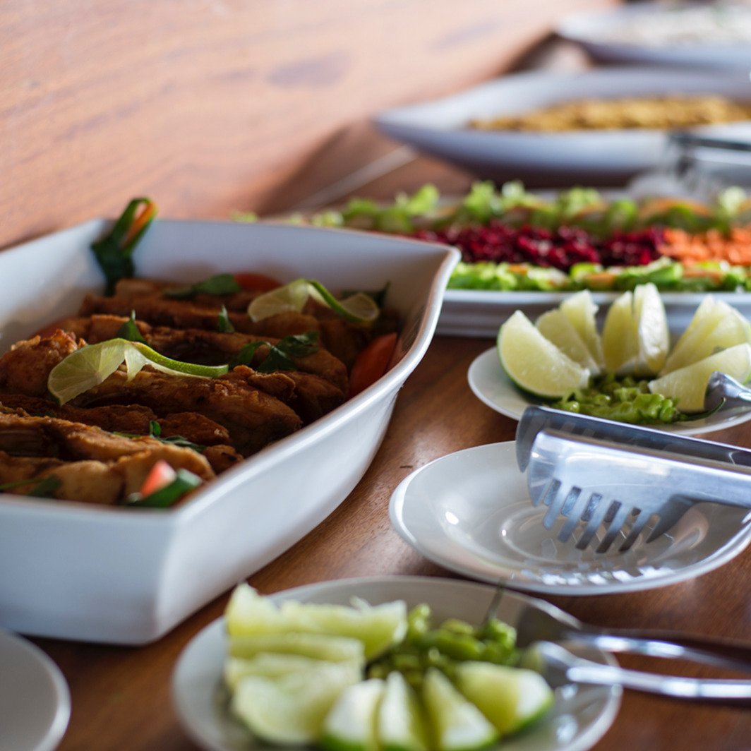 Every meal a celebration — vibrant, generous, and made for sharing. A buffet spread on a wooden table during an Amazon Cruise Trip in Brazil, featuring golden fried fillets garnished with lime wedges, a colourful vegetable salad with beetroot and carrots, and fresh cucumber slices served on white ceramic dishes