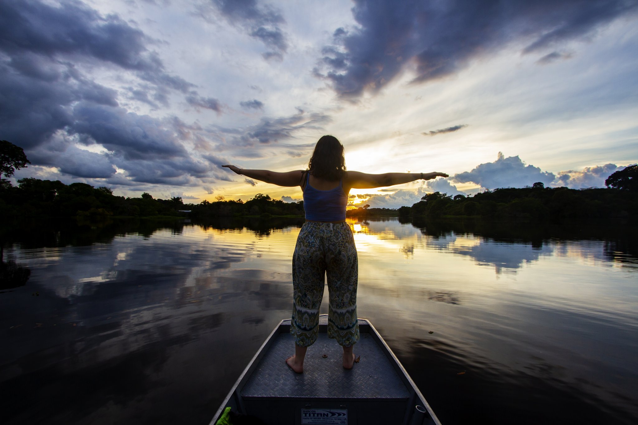Traveler standing on a boat bow with arms outstretched at sunset on an amazon jungle tour brazil river