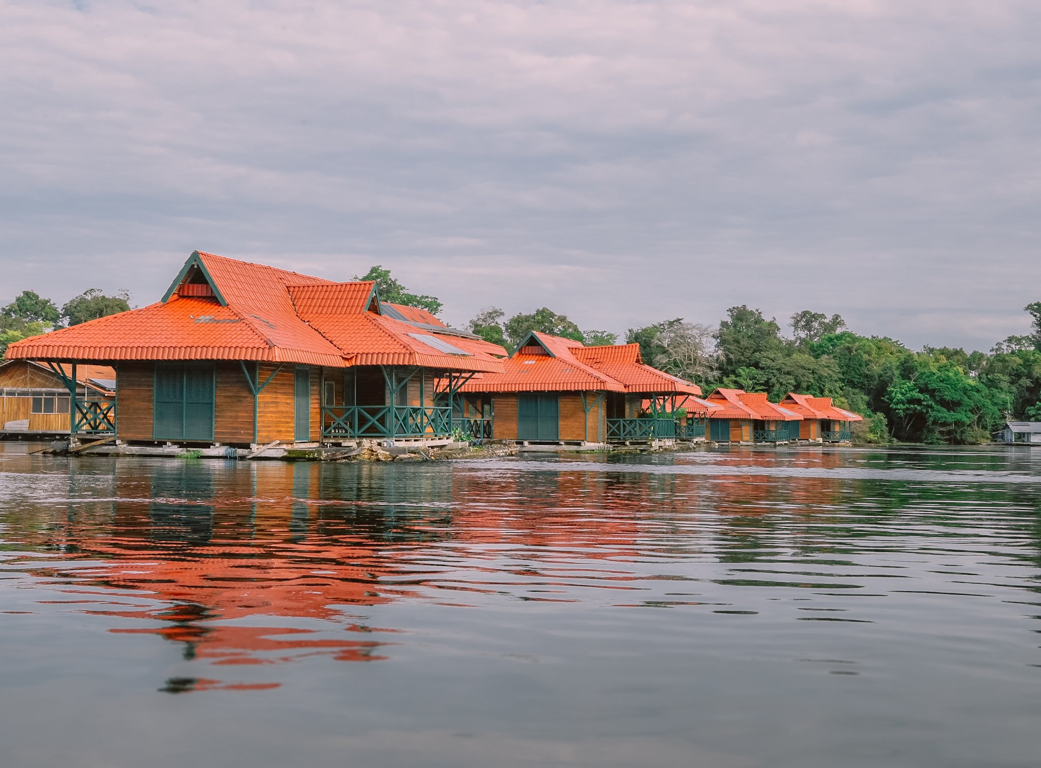 A row of wooden overwater cabins with vivid orange-tiled roofs reflected in calm river water, part of an amazon rainforest ecolodge trip in brazil surrounded by dense tropical forest