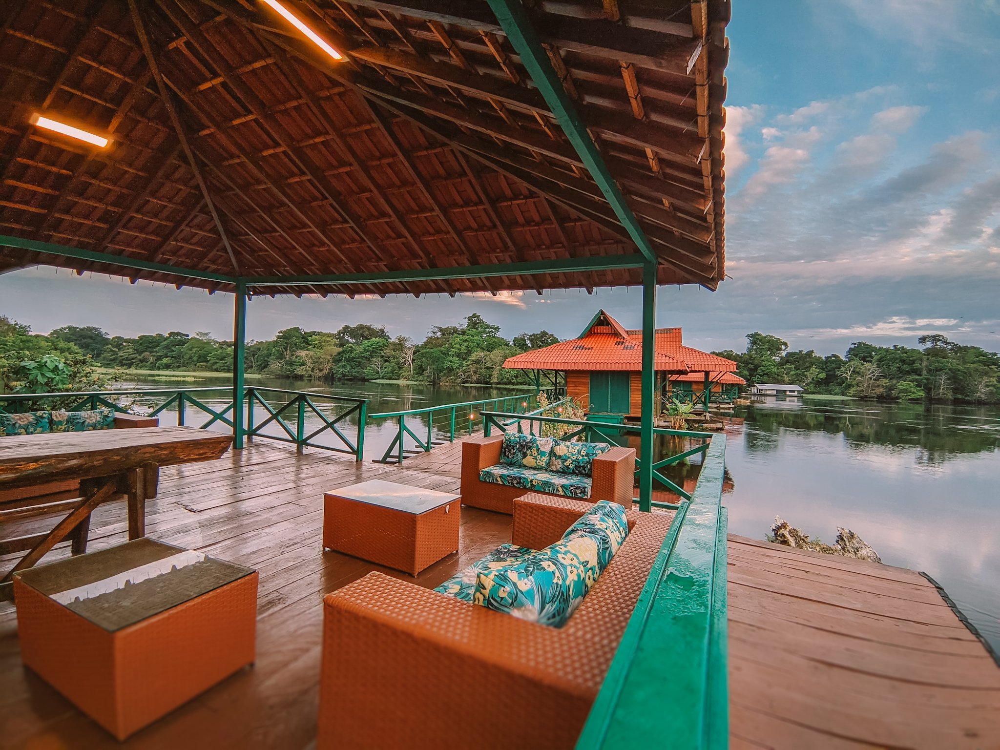 Covered wooden terrace with rattan lounge furniture overlooking a calm river and dense forest canopy at an amazon rainforest ecolodge trip in brazil