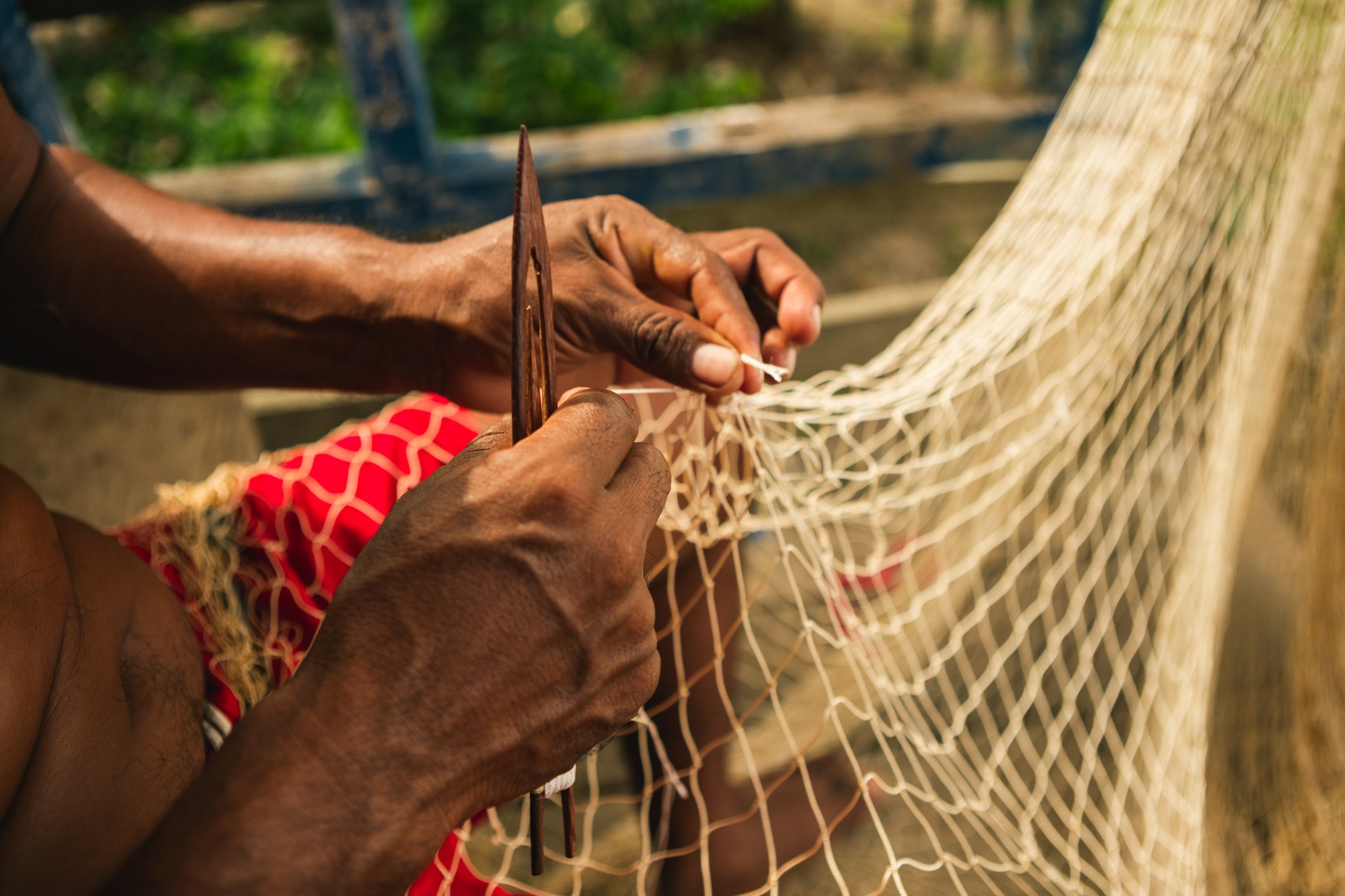 Close-up of skilled hands using a wooden needle to mend a fishing net during an amazon rainforest ecolodge trip in brazil, with green vegetation softly blurred in the background