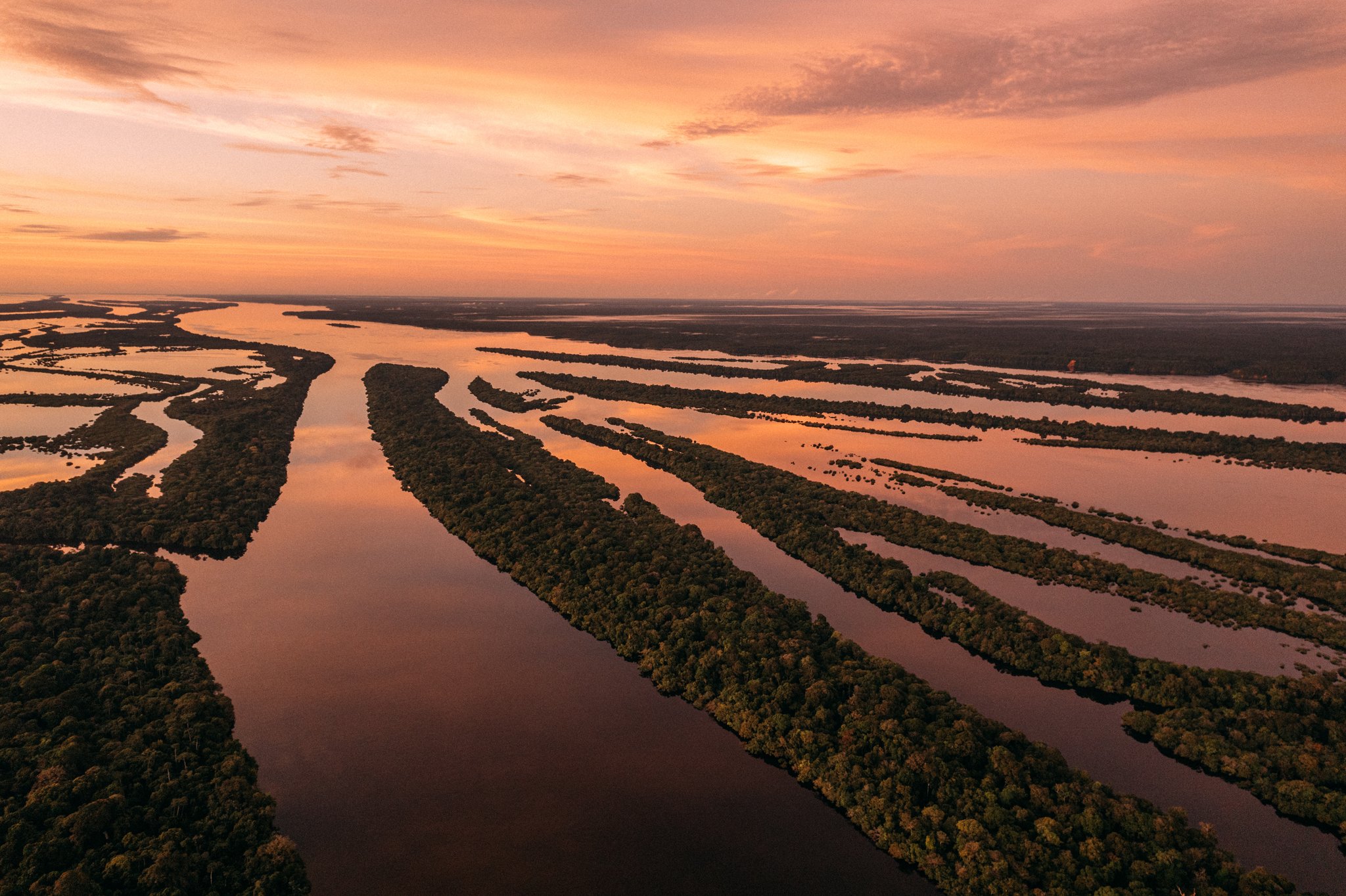 Aerial view of the Amazon rainforest tours Brazil region at sunset, showing winding river channels and flooded forest islands glowing under an orange sky