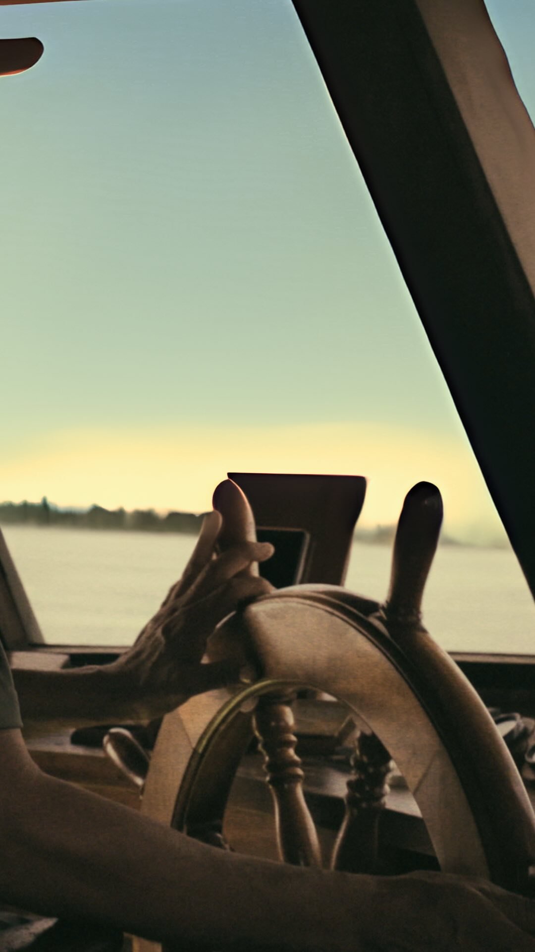 A hand rests on a wooden boat helm during an Amazon River Cruise Brazil journey, with calm open water and a soft dawn sky stretching ahead through the windscreen