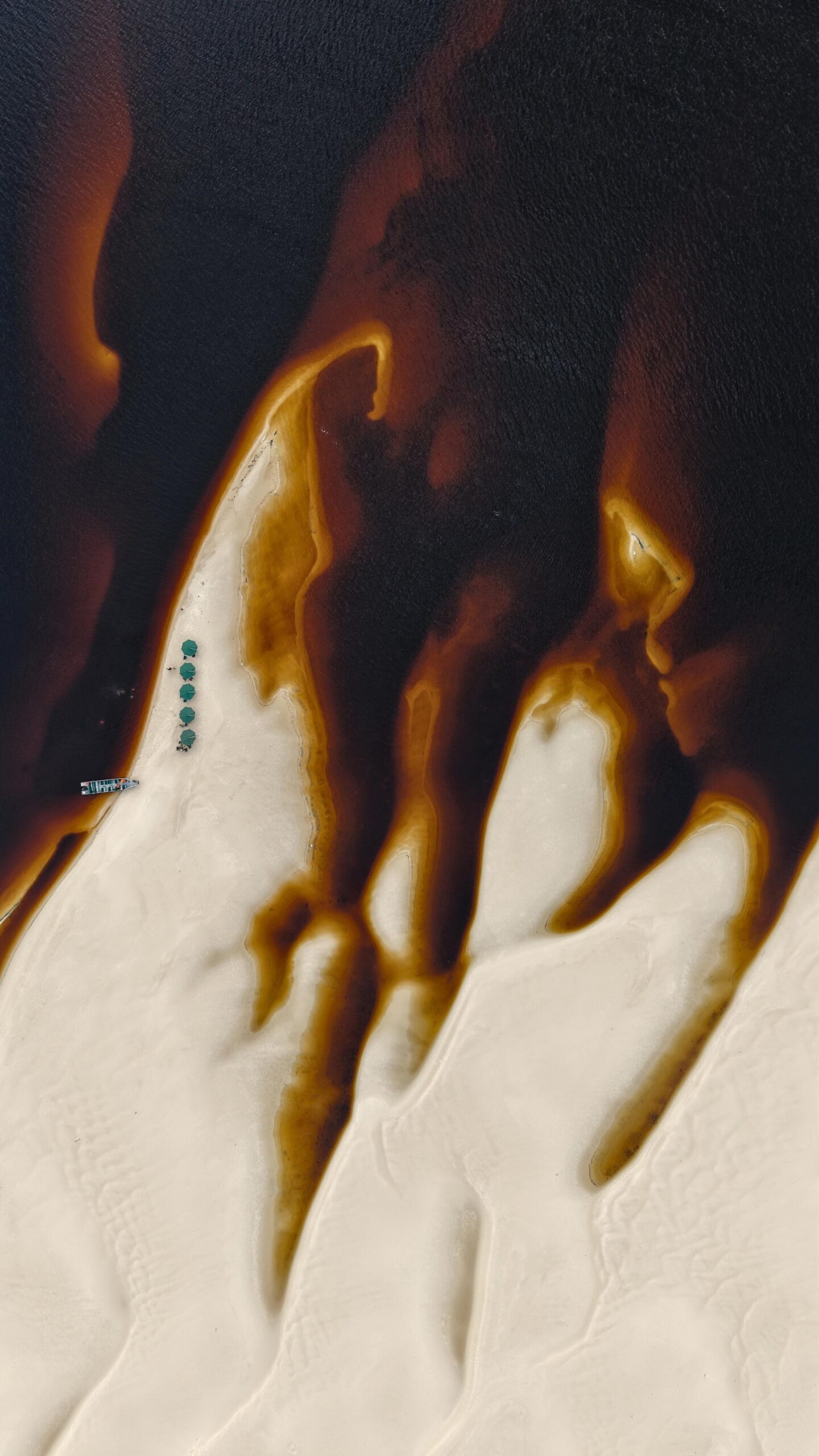 Dark water claws at white sand — nature's own abstract art, seen from the sky. Aerial view of a white sandbar finger extending into the dark tannin-stained waters of an Amazon River cruise Brazil route, with a small boat and green tents visible from above