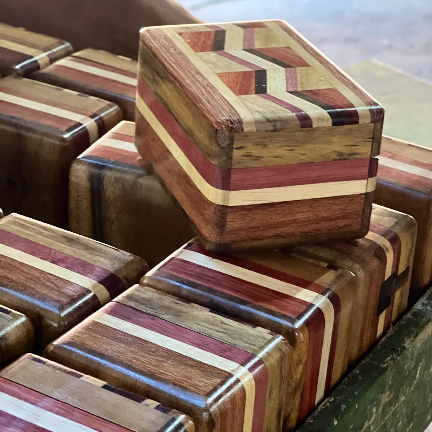 Polished stripes of purple, amber, and ebony — each box a different story to carry home. A collection of small handcrafted wooden boxes with inlaid multicoloured wood stripe patterns, stacked in a tray at a local artisan workshop on an Amazon River Cruise Brazil stop in Novo Airão