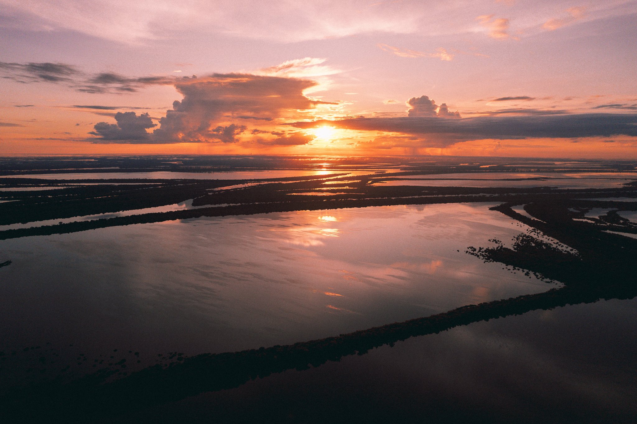 Fire in the sky, fire on the water — the Amazon floodplain at dusk stretches to the horizon. Aerial view of a vast flooded Amazonian floodplain at sunset, with orange and pink light reflected across interconnected waterways and dark forested islands, near Anavilhanas Jungle Lodge Brazil