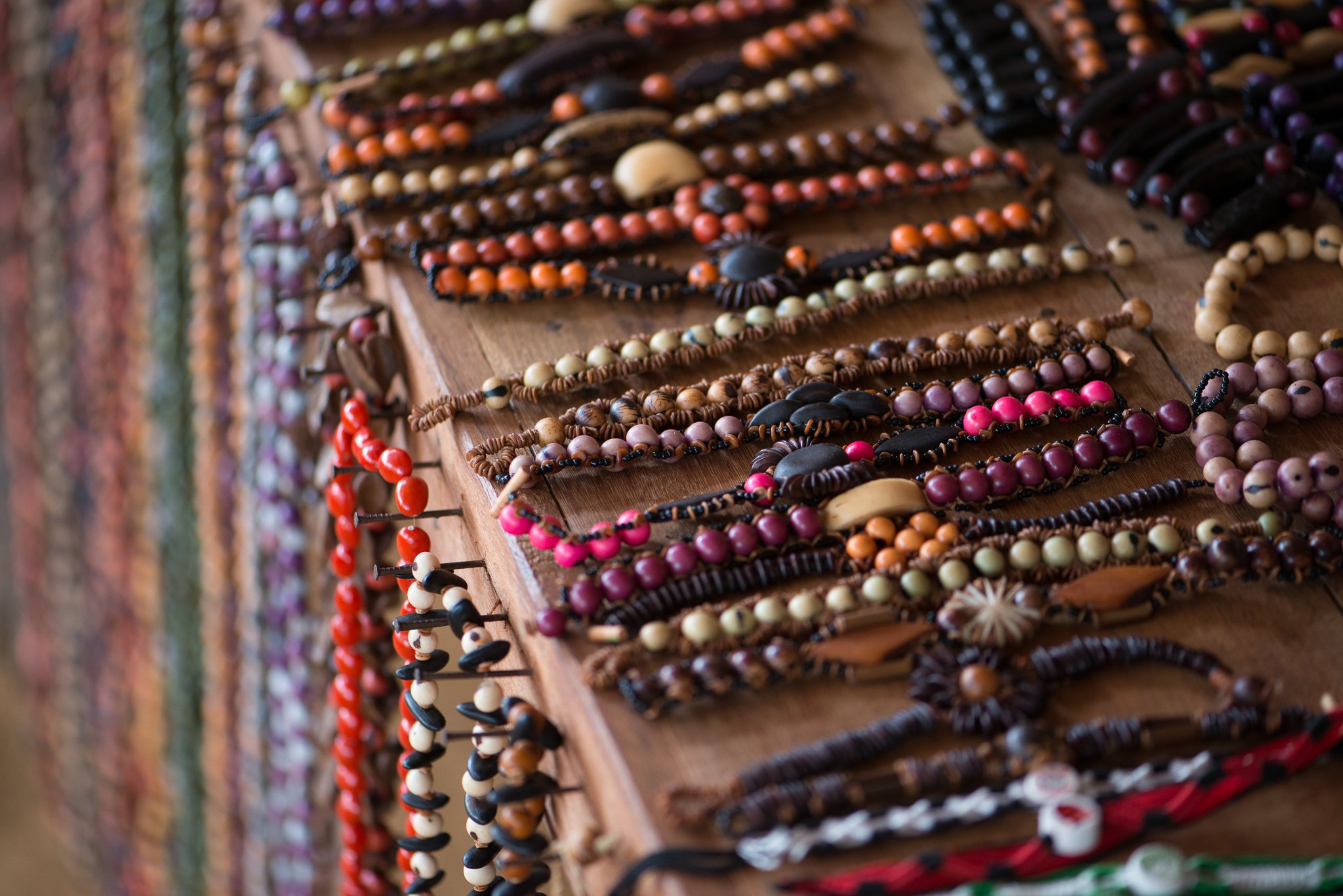 Handcrafted from forest seeds — every bracelet a small piece of Amazonian life to take home. Photo: MARCELO ISOLA Rows of handmade bracelets strung with colourful natural seeds and wooden beads displayed on a wooden board at a riverside community near Anavilhanas Jungle Lodge Brazil
