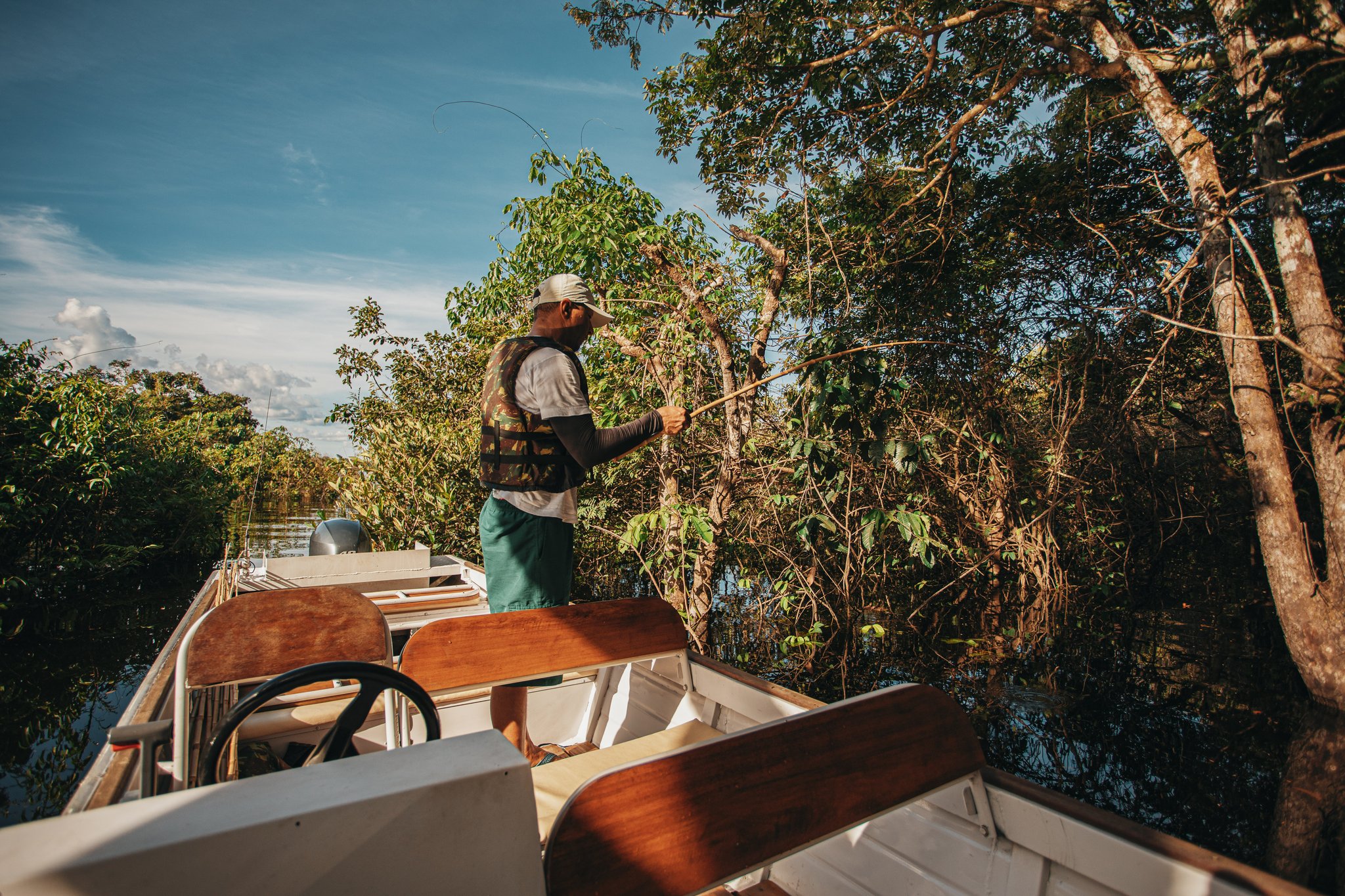 Rod bent, forest close — piranhas lurking just beneath the surface. Photo: Felipe Castellari A guide stands at the bow of a small motorboat, fishing rod in hand, casting toward dense riverside vegetation during a recreational fishing excursion at Anavilhanas Jungle Lodge Brazil