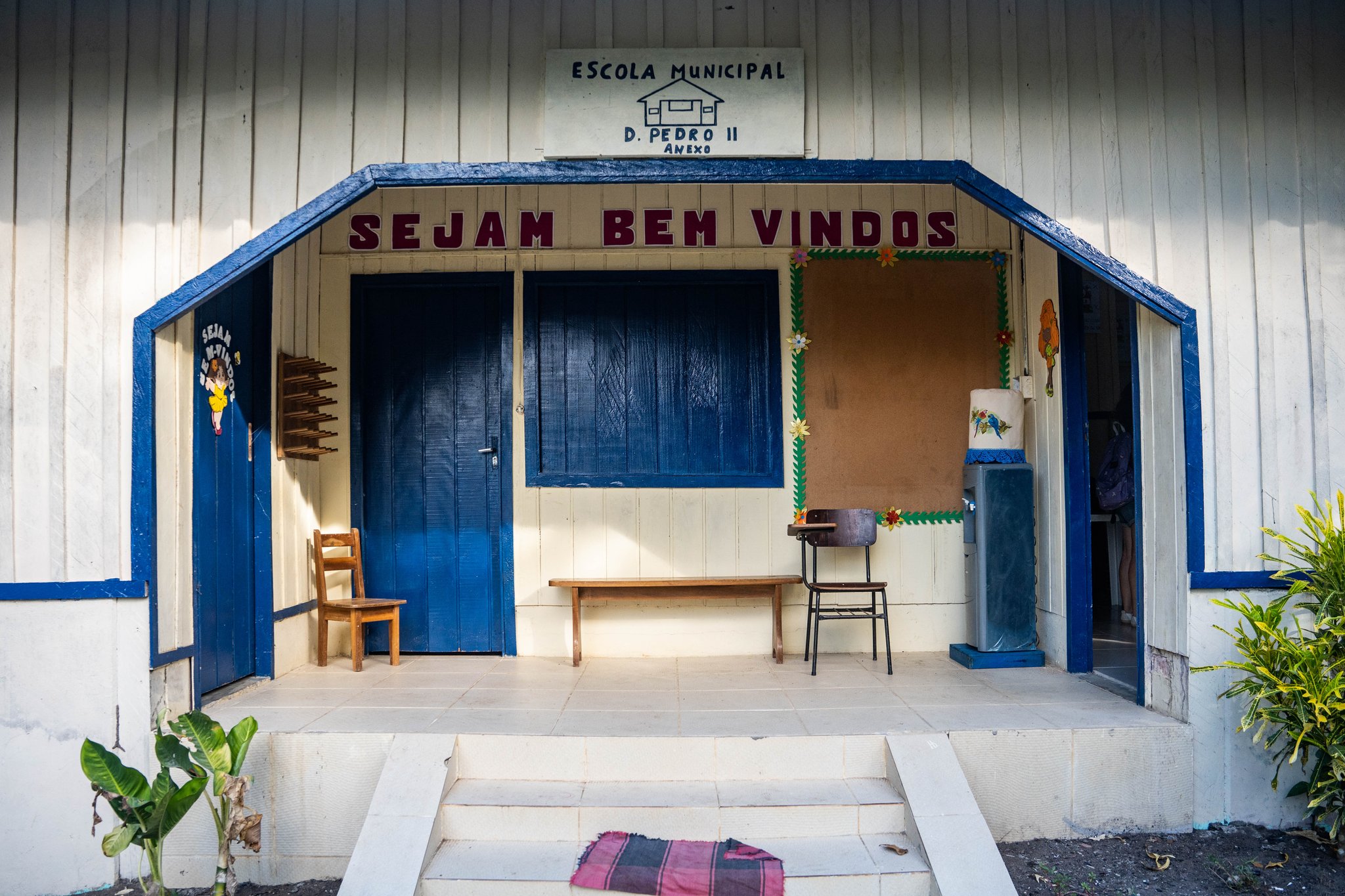 "Sejam Bem Vindos" — a warm welcome at the local school in an Amazonian riverside village. Entrance of Escola Municipal D. Pedro II, a white wooden community school with blue trim and a 'Sejam Bem Vindos' welcome sign, visited during an Anavilhanas Jungle Lodge Brazil riverside community excursion