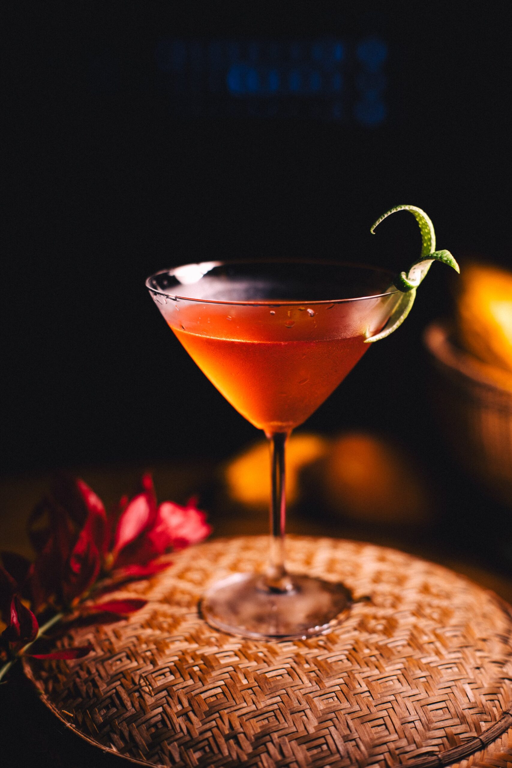 Crimson, citrus-kissed, and served under jungle darkness. A deep red cocktail in a martini glass garnished with a lime twist, resting on a woven tray beside a red tropical flower at Anavilhanas Jungle Lodge Brazil