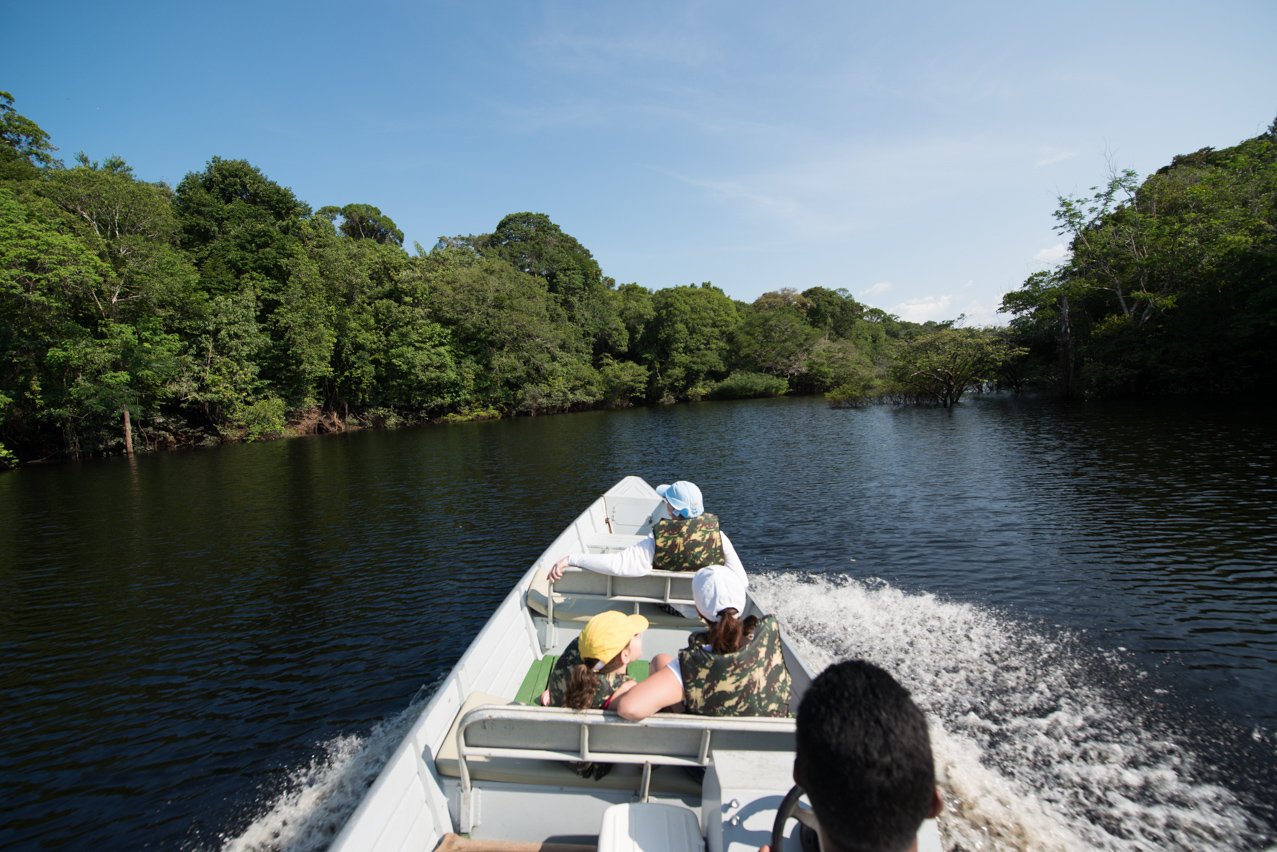 Engine roaring, the jungle parts — a speedboat cuts deep into the Amazon. Photo: MARCELO ISOLA Guests wearing life jackets speed along a dark-water Amazonian river on a motorboat excursion at Anavilhanas Jungle Lodge Brazil, with dense rainforest canopy lining both banks under a clear blue sky