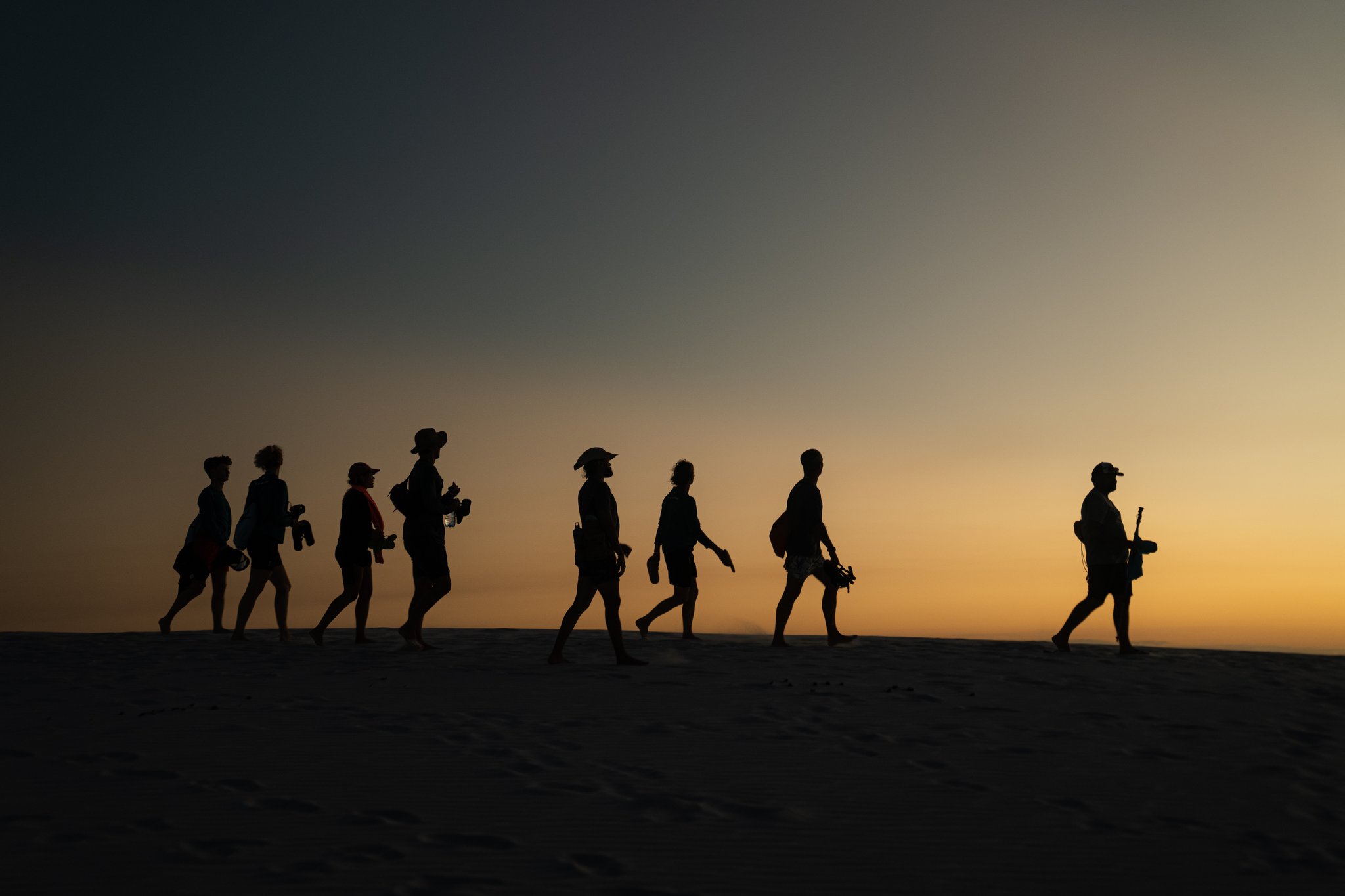 Eine geführte Gruppe wandert im Gänsemarsch über weiße Dünen im Sonnenuntergang — eine Wanderreise durch Brasilien in den Lençóis Maranhenses