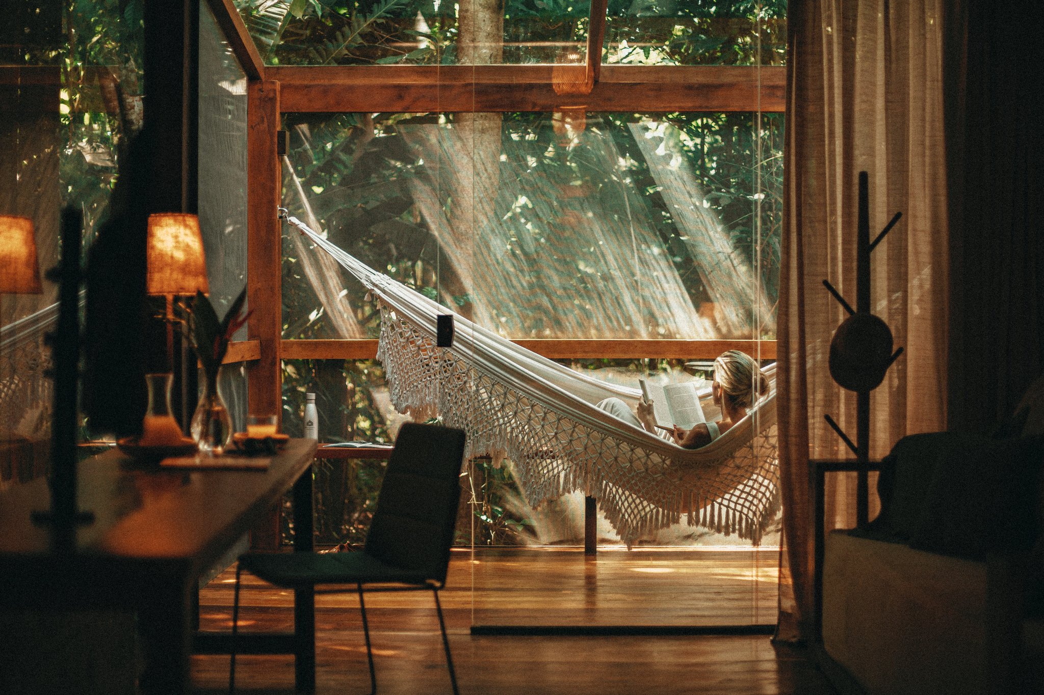 A woman reading a book in a macramé hammock on the sunlit terrace of a brazil luxury tours jungle lodge, surrounded by lush rainforest and warm timber interiors