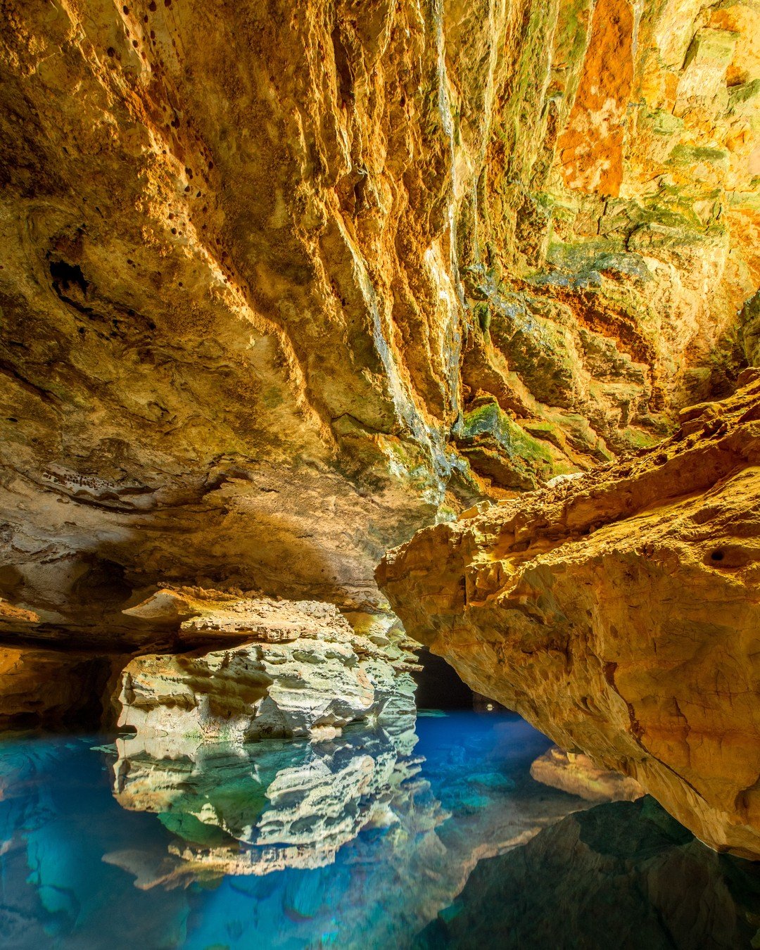Turquoise underground pool reflecting golden limestone cave walls on a Chapada Diamantina trip, with sculpted rock formations rising from mirror-still water
