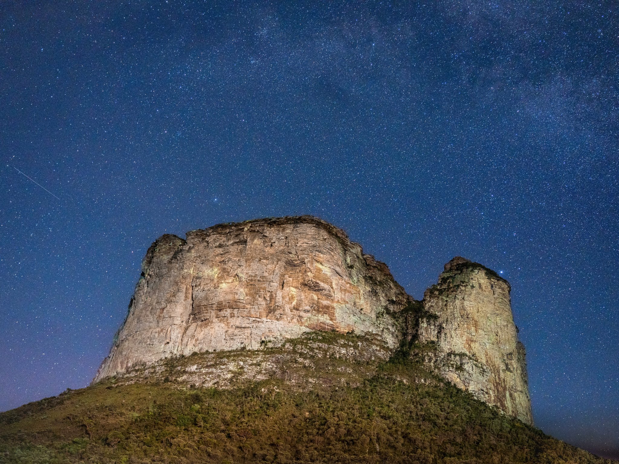 A massive sandstone butte lit from below against a deep blue night sky filled with Milky Way stars on a Chapada Diamantina trip