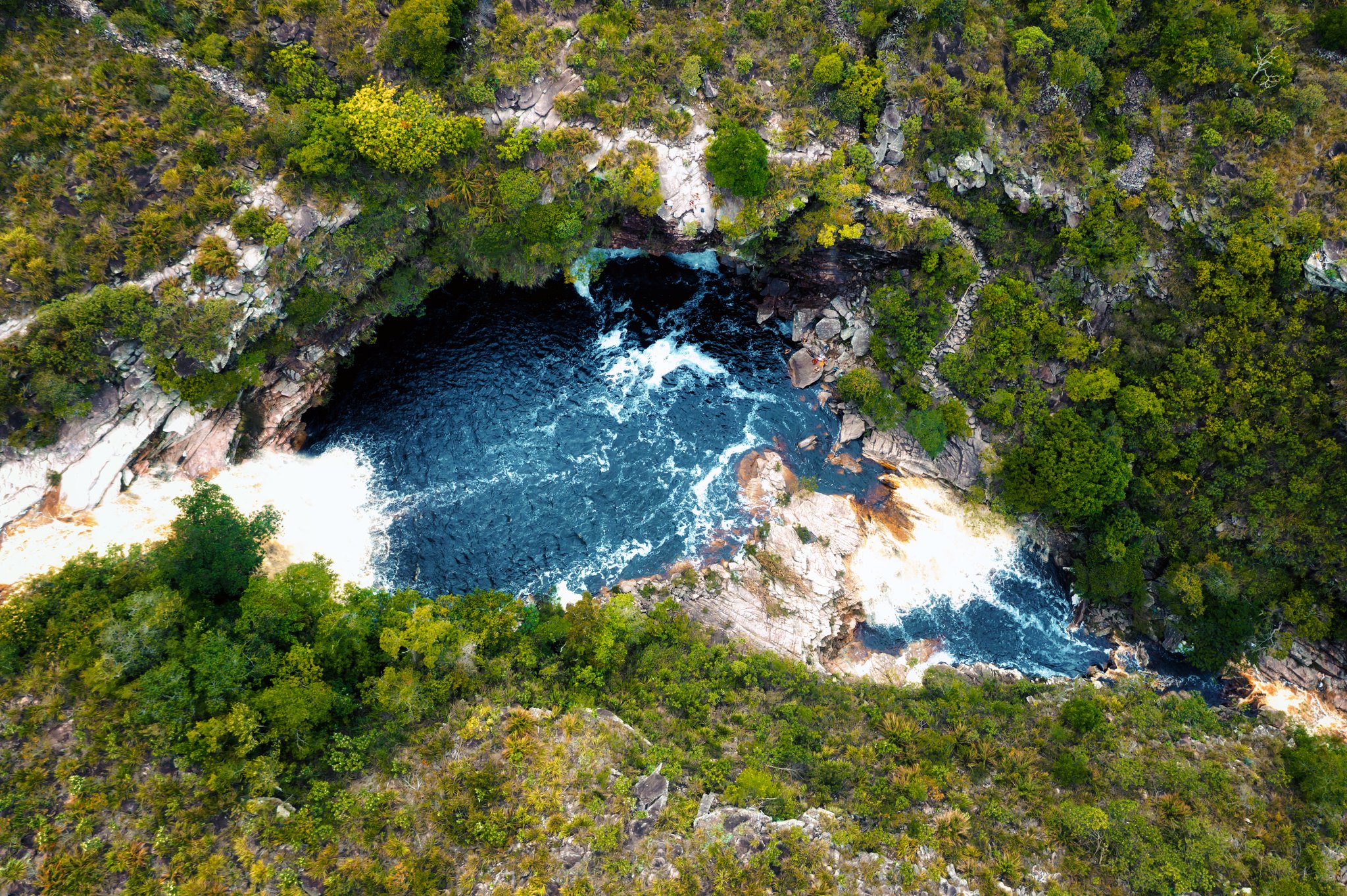 Aerial view of a deep blue natural pool carved into rocky outcrops surrounded by dense Cerrado scrub on a Chapada Diamantina trip