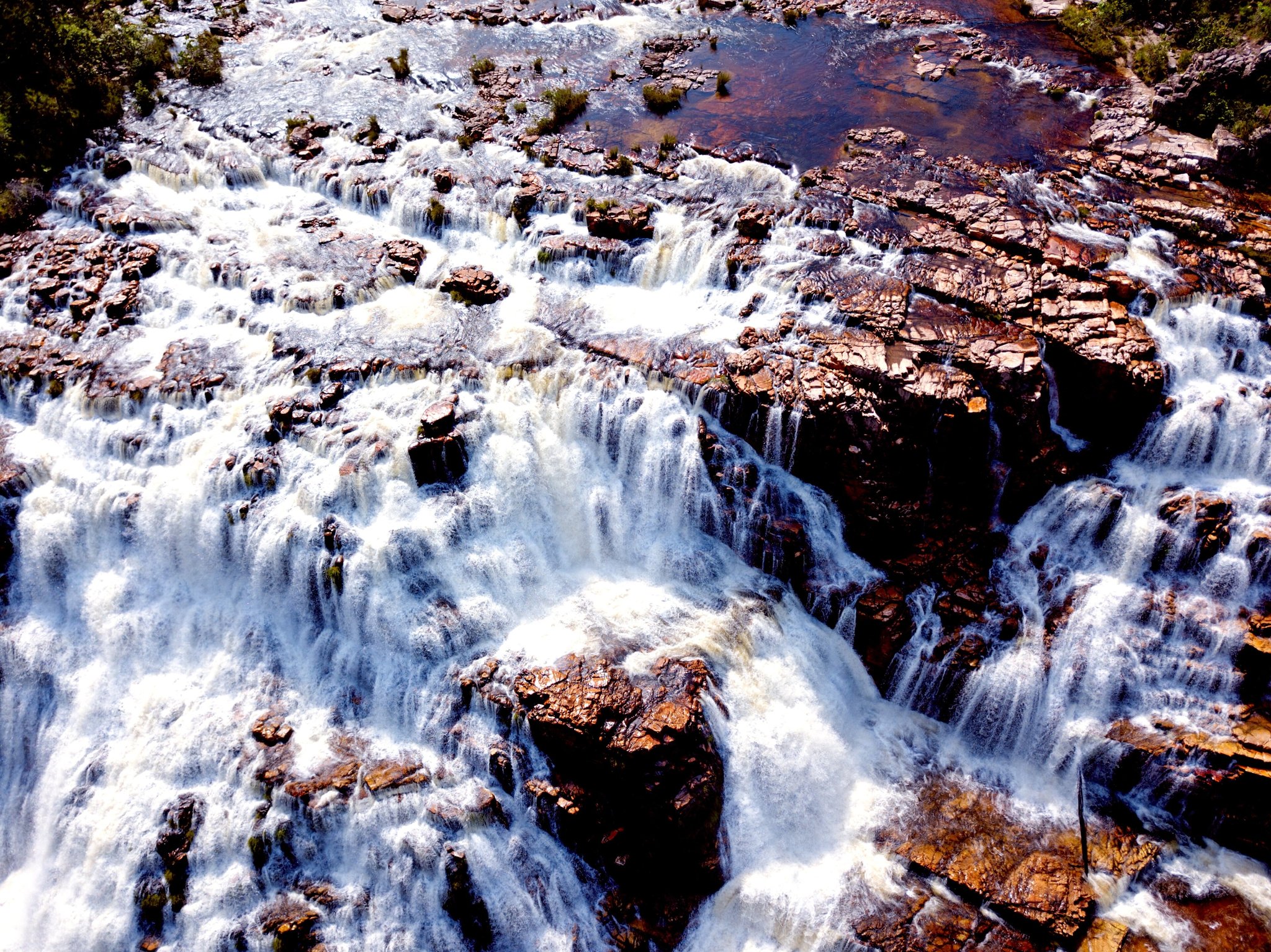 Aerial view of powerful white-water cascades rushing over layered iron-rich rocks in Chapada dos Veadeiros tours highlight area