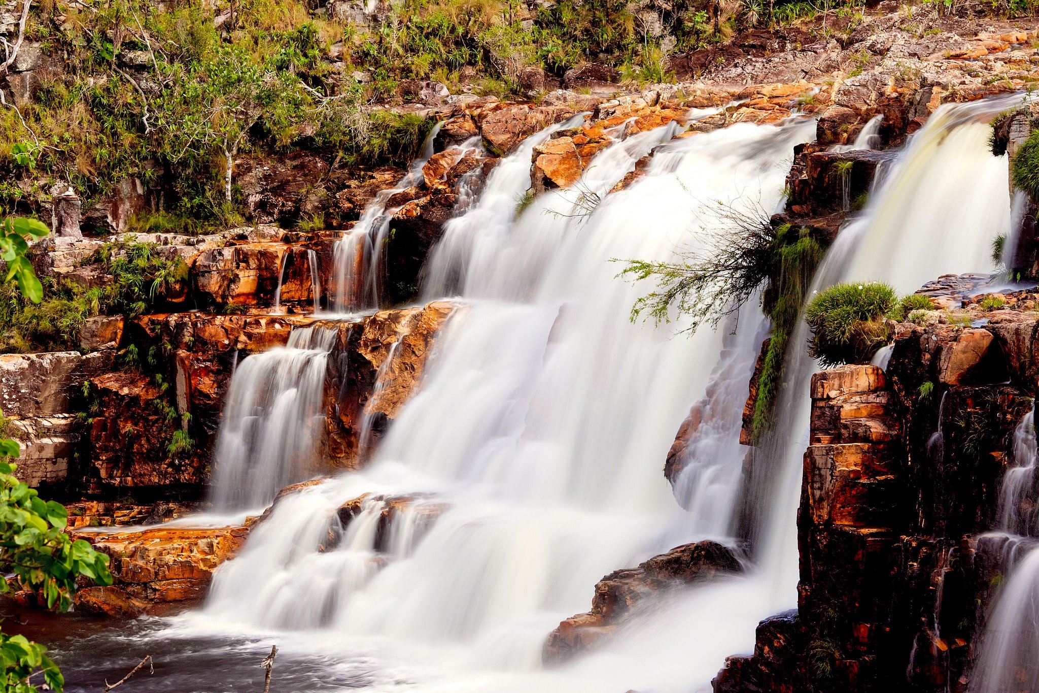Multi-tiered waterfall cascading over rust-coloured quartzite rock ledges surrounded by Cerrado vegetation in Chapada dos Veadeiros tours